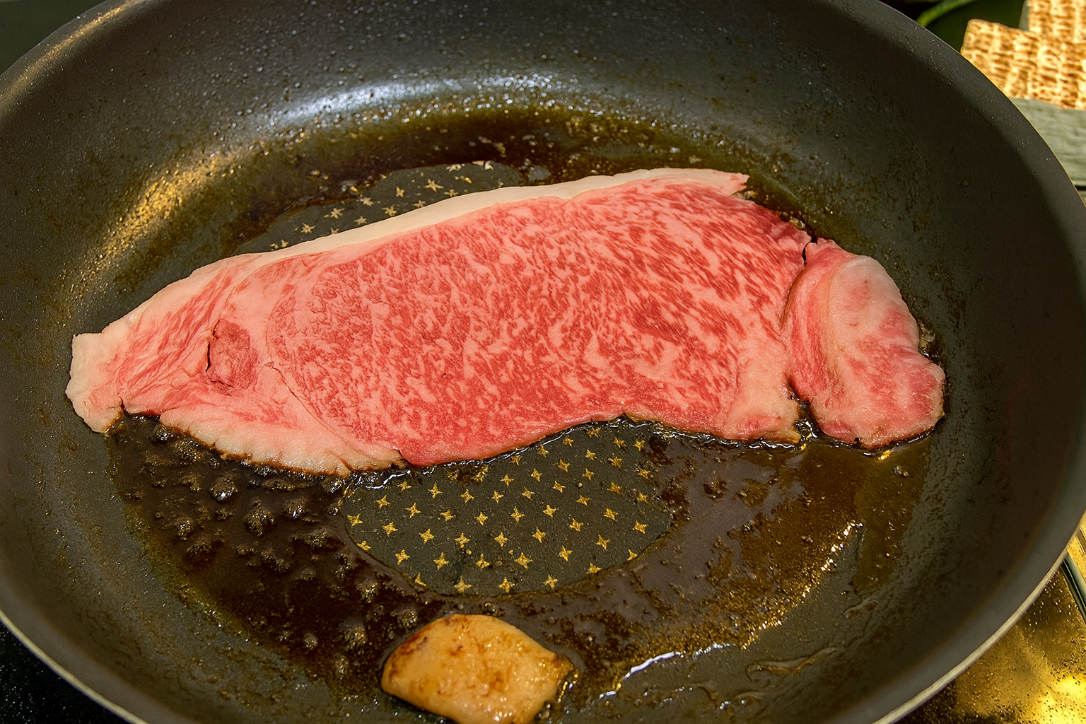 A slice of Nishinohara Wagyu sizzling in a hot pan with beef tallow for Kansai-style sukiyaki preparation.