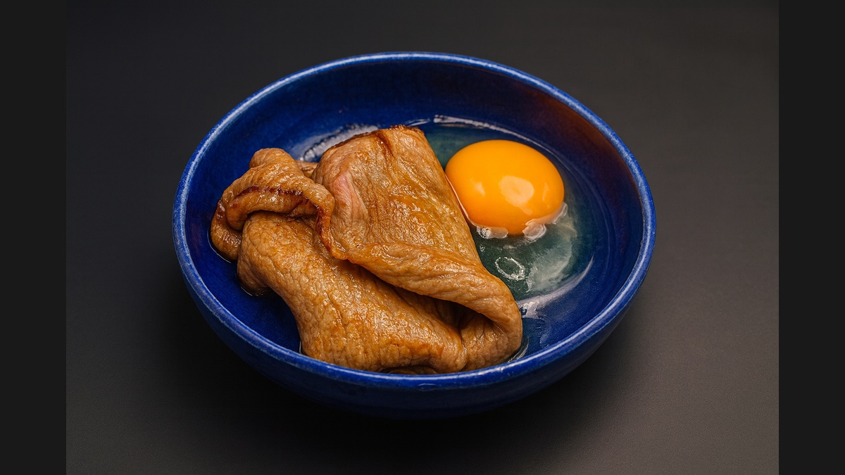 Sukiyaki-style Wagyu beef served with a raw egg yolk in a deep blue bowl.
